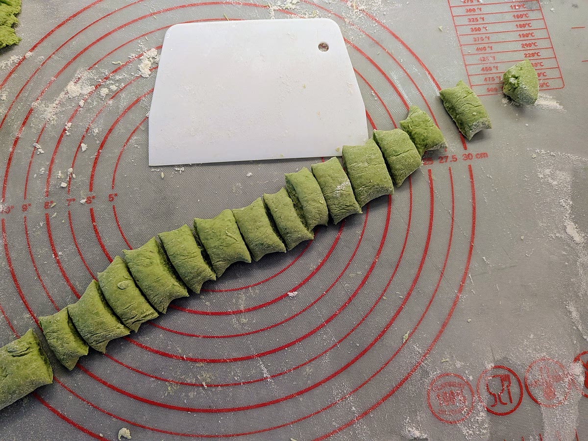 Cut the dough in 4, pick one part and roll it on the floured surface with your hands to make a slim snake. Cut the snake in 1 cm pieces.
Repeat for the other pieces of dough.