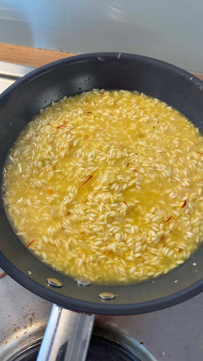 Cette étape concerne la cuisson du riz. Celui-ci doit frémir doucement (pas bouillir) tout au long de la cuisson. L’idée est de rajouter une louche de bouillon dès que la louche précédente a réduite. Comment savoir quand rajouter une louche ? Le riz doit être crémeux et se tenir, en le mélangeant on doit pouvoir voir le fond de la poêle pendant quelques secondes avant qu’il ne se referme.
Le riz ne doit jamais sécher.
Répéter l’ajout de louche jusqu’à ce que tout le bouillon y soit passé. Cette étape de cuisson peut durer jusqu’à 20 minutes.
Comment savoir que le riz est cuit ? Goûter, le riz doit être fondant mais il doit se tenir et ne pas faire une bouillie, il peut être légèrement plus dure vers le cœur pour une cuisson al dente.
Poivrer à votre convenance.
Lorsqu’il reste 1 minute de cuisson, ajouter les scampis dans le risotto et mélanger pour les réchauffer.