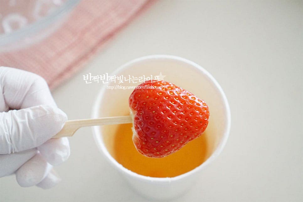꼬치에 끼워둔 딸기 또는 다른 과일에 설탕시럽을 입혀줍니다. 전체적으로 표면이 골고루 코팅되도록 뜨거울 때 넣었다가 빼주면 매끈하게 설탕이 입혀집니다. 식으면 모양이 울퉁불퉁해지니 뜨거울 때 만들어주세요. 시럽을 코팅하고 얼음물에 담갔다 빼면 사탕같이 바삭하게 굳어요. 물에 오래 담그면 녹을 수 있으니 냉기로 빠르게 굳혀줍니다.