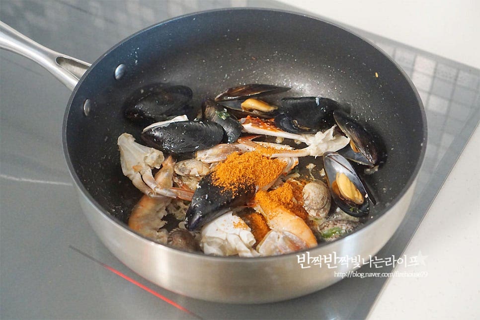 새우의 색이 주황빛이 되면 라면스프를 넣어줍니다. 기호에 따라 이 때 고춧가루를 넣어주어요. 스프는 해물의 간에 따라 2/3 정도 넣어주셔도 됩니다. 저는 스프를 다 넣고 나중에 물을 넉넉히 넣어주었어요. 스프를 먼저 볶아주어 매운맛 풍미도 살리고 해물의 감칠맛이 어우러지도록 해주었어요. 뜨거운 물 600ml 정도 부어줍니다. 물의 양은 간에 따라 가감하여 조절해 주세요. 뜨거운 물을 넣어주면 바로 끓어오르기도 하고 꽃게라면의 비린 맛을 잡아줄 수 있어요.