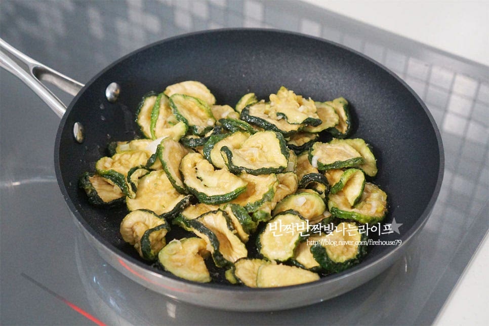 달군 팬에 식용유 2 큰 술을 두르고 밑간 한 호박고지를 넣고 가볍게 볶아줍니다. 전체적으로 윤기나게 코팅될 수 있도록 2~3분 볶아줍니다. 고르게 어우러지도록 저어가며 볶아줍니다. 멸치 다시마 육수 60ml를 부어줍니다. 육수 대신 물을 넣어도 좋습니다. 육수가 들어가면 보다 깊은 맛을 낼 수 있어요. 재료의 상태나 화력에 따라 육수의 양을 조절하여 촉촉하게 요리해 주세요. 뚜껑을 덮고 2분 정도 찌듯이 익혀줍니다. 수분이 골고루 어우러지면서 딱딱하게 마르지 않고 속까지 촉촉해집니다.