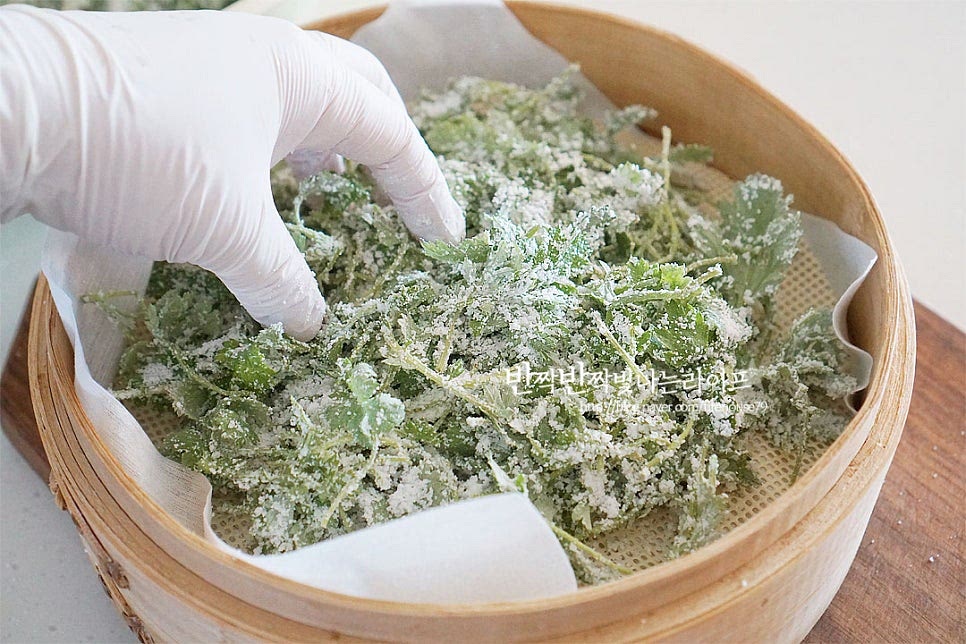 찜기에 면포와 실리콘 매트를 깔고 그 위로 쑥버무리를 올려줍니다. 자연스럽게 겹겹이 담아주셔야 사이사이로 뜨거운 공기가 들어가 찰지게 잘 익어요. 반죽이 많은 것 같다고 손으로 누르시면 안 됩니다. 수북하게 쌓인 것 같지만 익으면서 자연스럽게 줄어들어요.