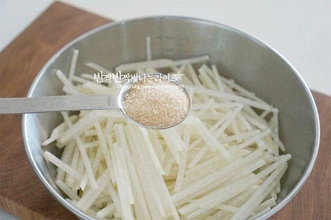 넉넉한 크기의 볼에 무채를 넣고 설탕 4 큰 술, 천일염 1/2 큰 술을 넣어줍니다. 소금 간은 조절해 주셔도 됩니다. 달콤 짭조름한 간을 먼저 해주어 쓴맛을 잡고 감칠맛을 더해줍니다. 조물조물 버무려줍니다. 버무리다 보면 가루 입자가 녹으면서 물이 촉촉하게 생겨요.
