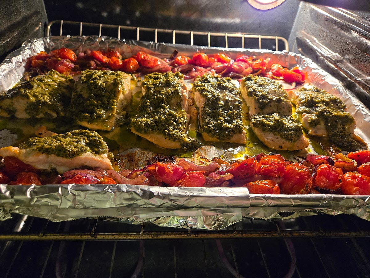 Remove the sheet pan from the oven and move the tomatoes and onions to the outsides to make space for the salmon in the center. Arrange the salmon fillets down the center of the baking sheet, skin-side down.
