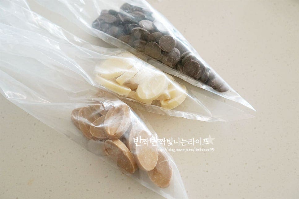 초콜릿 장식을 해줍니다. 세 가지 종류를 준비해 주었으며 코팅과 커버춰 초콜릿을 섞어 만들어도 좋아요. 간편하게 만들 수 있도록 짤주머니에 초콜릿을 넣고 따뜻한물에 담가 중탕으로 녹여줍니다. 물이 들어가면 코팅이 되지 않으니 들어가지 않도록 해줍니다. 골고루 녹을 수 있도록 짤주머니를 위아래로 섞어가며 녹여주었습니다. 녹으면 높이가 비슷한 컵에 넣고 손잡이 부분을 제외한 부분으로 초코코팅을 해줍니다. 너무 두껍지 않게 살살 털어가며 발라주세요. 종이호일 위에 일정한 간격을 두고 올린 뒤 토핑 재료를 뿌려준 뒤 굳혀줍니다. 여러가지를 곁들여주면 보기에도 먹음직스러우며 다채롭게 맛볼 수 있습니다. 빼빼로 포장 빼빼로데이 선물을 하기 위해 포장을 할 때는 감성 한스푼을 더해 종이박스에 담거나 OPP 비닐봉지에 모양이 잘 보이도록 담아 주변에 마음을 선물하면 좋답니다. 길이가 맞는 비닐에 담아주면 모양이 고정되어 보기에 좋아요. 기다란 막대과자에 달콤한 초콜릿과 토핑 재료가 더해져 골라 먹는 즐거움이 가득해요. 기본 초코도 맛있지만 예쁜 색감과 식감을 더해주면 더욱 맛나요. 영상도 같이 담았어요. 바삭 고소하고 달콤한 수제 빼빼로로 빼뻬로데이 선물을 준비해 보시는 건 어떠세요. 직접 만들어 맛도 좋고 정성이 느껴진답니다^^ 끄읕 !