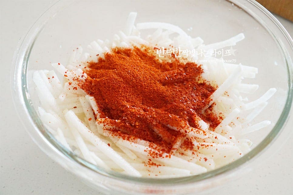 수분이 생겨서 촉촉한 그 상태로 고춧가루 5 큰 술을 넣어줍니다. 생채에 버무려 고춧가루가 물들면서 색을 빨갛게 내고 수분을 어느 정도 잡아줄 수 있도록 해줍니다. 양조간장 2 큰 술, 액젓 1 큰 술 식초 3 큰 술을 넣어줍니다. 이때 진간장으로 대체 가능하며 검게 색이 스며들지 않도록 겉 테두리 쪽으로 간장을 둘러 넣어줍니다. 액젓 또한 까나리가 아닌 꽃게, 멸치 등을 넣어도 좋습니다. 골고루 간이 스며들 수 있도록 버무려주세요. 절인 뒤 버무려서 간도 잘 스며들고 부서지지않고 탱탱해요. 대파도 넣고 함께 버무립니다. 물이 생기면 싱거워질 수 있어 천일염 한 꼬집을 더해주는데요. 소금 간은 입맛에 맞게 조절해야 짜지 않으면서 신맛, 단맛이 적당하게 어우러집니다. 새콤하게 드신다면 식초를 더해도 좋고요.