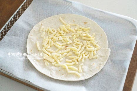 또띠아 위로 피자 재료들을 올려줍니다. 먼저 트레이 위에 한 장을 올린 뒤 치즈를 약간 뿌린 뒤 한 장 더 올려줍니다. 치즈크러스트 같은 느낌으로 두장을 겹쳐주었어요. 토마토소스 1 큰 술을 넓게 펴발라줍니다. 간에 따라 짜지 않게 양을 조절해 주세요. 바질페스토 1 큰 술도 발라줍니다. 직접 만든 바질페스토라 조금 넉넉히 넣었는데 입맛에 따라 양을 조절해주세요. 바질소스를 생략하고 토마토소스 위에 토핑재료를 듬뿍 올려주셔도 좋습니다. 그 위로 치즈를 뿌리고 토마토를 올려줍니다. 방울토마토를 구워서 먹으면 단맛이 풍부해져 잘 어울립니다.