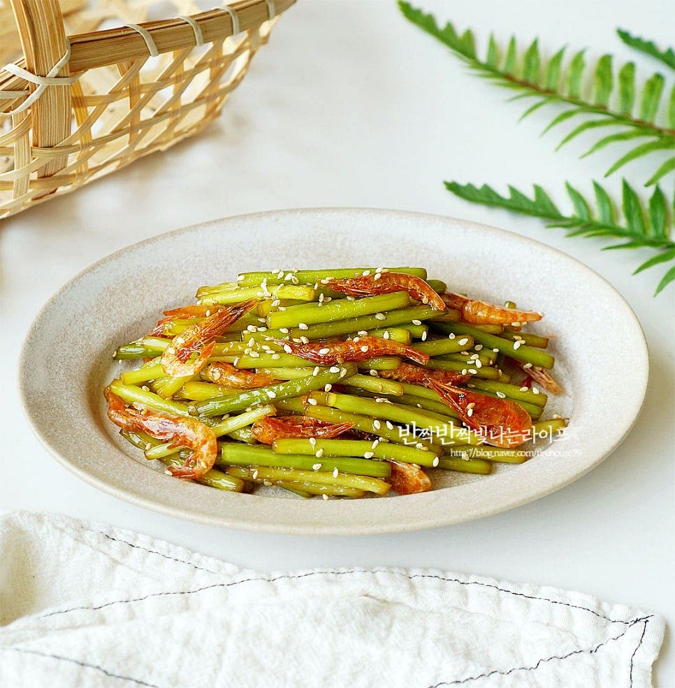 아삭하고 부드러운 마늘쫑과 바삭하고 짭조름한 건새우가 고소하게 어우러지게 완성입니다. 마지막에 푸짐하게 담아 통깨를 뿌려주면 맛있어 보입니다. 영상도 같이 담아주세요. 한창 국산 마늘쫑이 나오는 시기라 제철 반찬으로 만들어 먹음 밥 한 그릇 뚝딱 먹게 된답니다. 마늘종에 간이 맛있게 밸 수 있도록 볶은 뒤 건새우와 고소한 감칠맛으로 마무리하면 간단하면서도 맛있게 맛볼 수 있어요. 맛있는 제철 요리 만들어드세요. 끄읕 !
