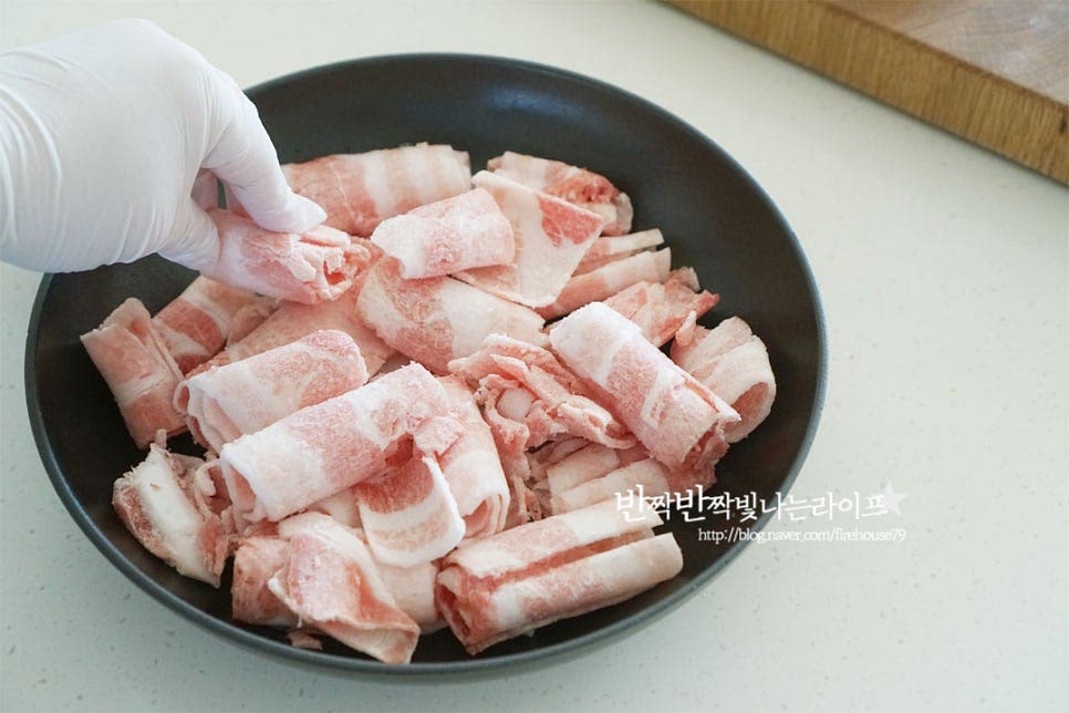 깊이가 있는 팬 또는 냄비에 대패삼겹살을 먼저 담아줍니다. 살코기와 지방이 적당하게 어우러져 고소한 풍미를 더욱 풍성하게 해주고 돼지고기를 넣으면 보다 푸짐하게 맛볼 수 있습니다. 그 위로 자른 두부를 올려줍니다. 양념이 잘 스며들 수 있도록 펼쳐서 담아줍니다. 대파와 고추도 같이 넣어주세요.