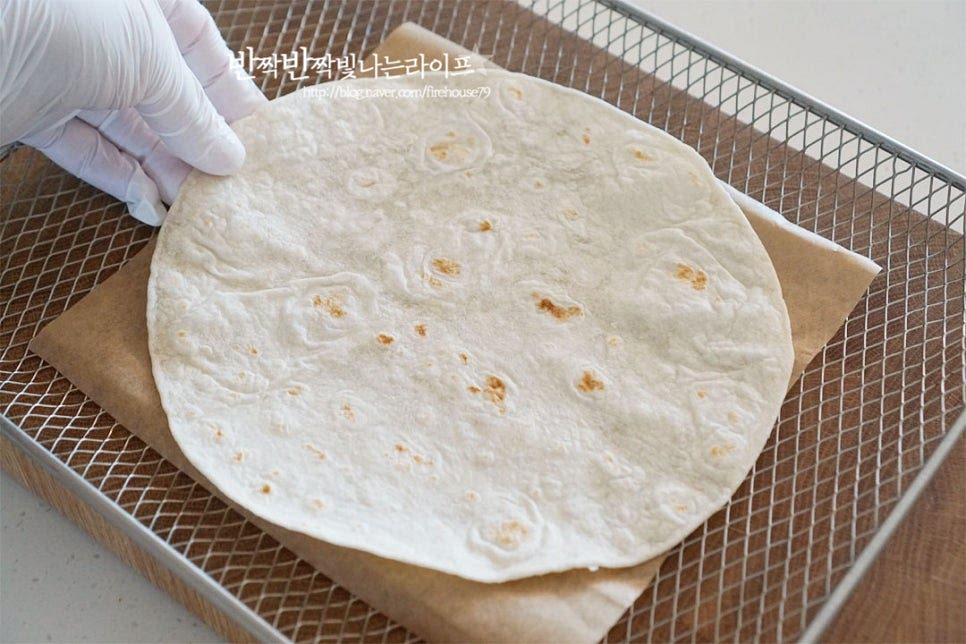 종이호일이나 트레이를 먼저 깔고 그 위로 또띠아를 올려줍니다. 집에서 피자만들기 할 때 밀가루에 이스트를 넣고 직접 도우를 반죽할 수도 있지만 얇게 만든 토르티야 하나면 누구나 쉽게 만들 수 있어요. 담백 고소한 맛으로 토핑 재료들과 잘 어울리며 구웠을 때 바삭바삭한 식감이 맛이 좋아요. 그 위로 치즈 1/3분량을 넓게 뿌려줍니다. 다시 토르티야로 덮어줍니다. 한 장으로 만들 수 있지만 두께가 얇고 햄이 짠맛이 있기 때문에 두 장을 겹쳐 도우 대신 활용해 주었답니다.