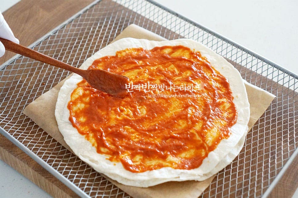 도우 위로 토마토소스를 골고루 발라줍니다. 안쪽으로 1~2cm 여유를 두었어요. 시판용 소스나 토마토소스면 됩니다. 나머지 치즈 2/3를 넓게 올려줍니다. 너무 많이 넣으면 흘러내릴 수 있어서 가운데를 중심으로 끝부분은 여유를 두고 토핑해요. 페퍼로니 피자 만들기