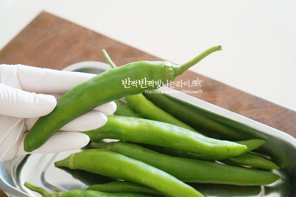 아삭이고추 8개 정도를 준비했습니다. 일반적인 것 보다는 크기가 크고 수분이 많기 때문에 먹을 만큼 바로 무침 반찬 만들어 먹어야 물이 생기지 않고 양념맛도 진하고 식감이 좋습니다. 꼭지 부분을 잡아당기면 손쉽게 분리가 됩니다. 재료를 식초물에 담가 살짝 흔들어 준 뒤 흐르는 물에 헹구어주세요. 물에 오래 담그면 영양성분이 빠지니 가볍게 흔들어 씻어줍니다. 키친타월에 올려 물기를 꼼꼼하게 제거해 줍니다.