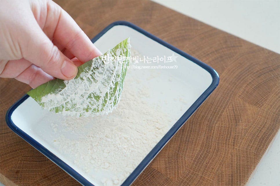 거친 뒷장에 부침가루를 약간 묻혀줍니다. 전을 구울 때 모양이 풀리지 않고 고정될 수 있도록 살짝만 묻혀 털어주세요. 뒷면 위로 맛살을 올린 뒤 감싸서 모양을 잡아줍니다. 크기가 큰 것은 크기에 맞게 잘라서 말아주면 먹음직스럽게 잘 어우러집니다.