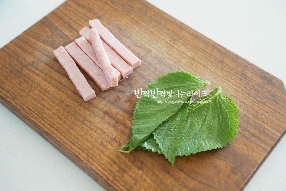 스팸은 1~1.2cm 두께로 잘라주고, 깻잎은 꼭지를 제거하고 반으로 잘라줍니다. 꼬마김밥은 크기가 작기 때문에 속재료를 먹기 좋게 작은 크기로 준비해 주는데요. 단무지는 길이를 반으로 자른 뒤 굵기도 반으로 잘라줍니다. 달걀은 소금 약간 넣고 곱게 풀어주어요. 달군 팬에 식용유를 두르고 풀어둔 계란물을 부어 지단을 구워줍니다. 햄과 비슷한 두께로 만들고 싶어 조금 두툼하게 구워주었어요. 길이가 짧은 형태이기 때문에 사각 팬을 활용하여 구워주시면 일정한 크기로 자르기 편해요. 타지 않고 속까지 부드럽게 익히기 위해 중약 불로 불 조절을 하여 구워줍니다. 구운 뒤 8등분 하여 썰어줍니다. 팬을 키친타월로 정리한 뒤 스팸을 노릇하게 구워줍니다. 햄 자체의 짠맛이 있는 편이라 따로 간을 하지 않고 구워주었어요. 식용유를 두르지 않아도 잘 구워집니다. 스팸, 단무지, 계란, 깻잎 4가지의 기본과 함께 선택 재료로 슬라이스치즈를 넣어도 좋아요. 치즈는 2등분으로 잘라 주었습니다.