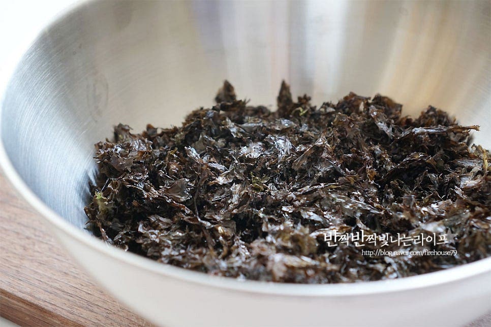 자반용 김을 준비했어요. 자반용이 아니라면 먹기 좋도록 잘게 찢어 준비해요. 작은 크기여야지 골고루 볶기도 좋고, 먹기도 좋답니다. 볼에 김을 넣은 뒤 카놀라유 1½ 큰 술, 참기름 2큰술을 고르게 뿌려주며 버무려줍니다. 김가루 만들 때 카놀라유가 아니더라도 향이 없는 식용유를 넣어주심 되며, 참기름 대신 들기름을 준비하셔도 됩니다. 소금 2/3 큰 술도 같이 넣어줍니다. 소금은 입자가 굵은 걸 넣으면 잘 녹지 않아서 얇은 걸로 넣어주었어요. 감칠맛을 살리고 싶다면 맛소금을 넣으셔도 좋아요~ 재료가 뭉치지 않도록 수저로 고루 저어가며 버무려주었어요. 먼저 간을 한 뒤 볶아주면 간도 잘 스며들고, 볶을 때 여유가 있어 타지 않게 볶기 편해요.