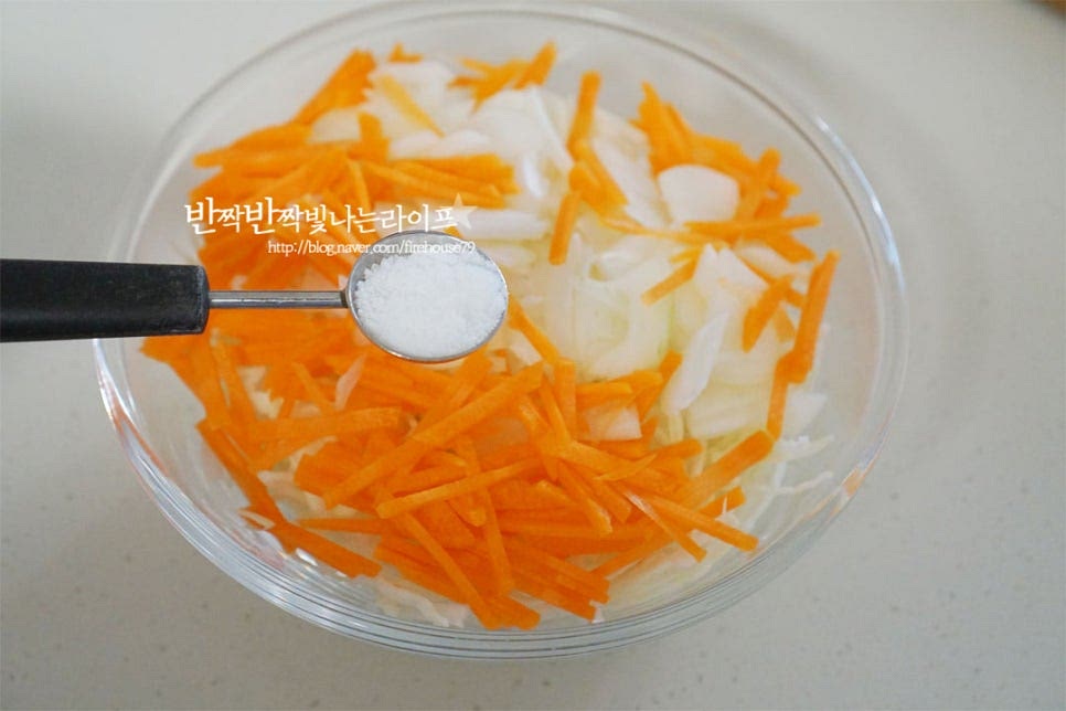 소스에 바로 버무리지 않고 아삭아삭한 식감을 살리기 위해 소금에 절인 뒤 샐러드를 만들 것이에요. 큼직한 크기의 볼에 채 썬 양배추와 재료를 넣고 소금 2/3 작은 술을 뿌려줍니다. 소금이 버무려지도록 저어줍니다. 중간에 한두 번 뒤적여주면서 20분 정도 절여줍니다. 20분이 지나면 숨이 죽고 수분이 나오면서 아작아작 식감이 느껴집니다. 절인 뒤 드레싱에 버무려 차갑게 먹으면 물이 생기지 않고 맛있게 먹을 수 있어요. 면포에 넣고 물기를 꼭 짜서 수분을 제거해 줍니다.