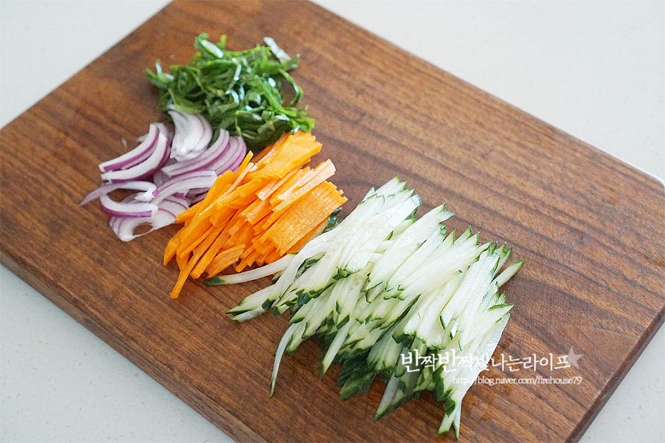 비빔만두에 들어가는 야채는 아삭한 식감이 있는 생채로 다양하게 넣어 만들면 푸짐하게 맛볼 수 있는데요. 냉장고 속 자투리 재료를 활용하면 좋아요. 양념장에 비벼서 먹는 메뉴인만큼 모든 재료를 곱게 채를 썰어줍니다. 양파는 매운맛이 난다면 찬물에 5분 정도 담가 헹구어주고, 당근과 오이는 어슷하게 썰어 자르고, 깻잎은 반으로 자른 뒤 채 썰어요. 길이 밸런스를 맞추어주면 먹기 좋습니다. 빠질 수 없는 양배추와 적채도 얇게 채를 썰어 줍니다. 달큰하고 아삭한 양배추가 정말 잘 어울려요.