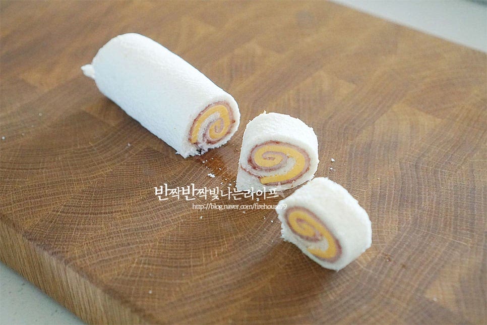 랩을 풀어보면 딱 알맞게 고정되어있어요. 그럼 한 입 크기로 일정하게 잘라줍니다. 단면이 달팽이모양처럼 겹겹이 말려있으면 먹음직스럽게 완성이에요. 한 입 크기라 집어먹기도 좋으며 아이들이 좋아하는 맛과 모양이라 간식 또는 도시락 메뉴로 요리하기 좋답니다. 그대로 올려두고 먹어도 되지만 나무 꼬치를 활용하여 꽂아주면 하나씩 쏙 빼서 먹기도 좋고 롤이 풀리지 않고 고정되어 편해요. 아이 간식으로 만든 것이라 귀여운 동물포크도 꽂아주었더니 먹음직스러워 보이죠. 우유와 같이 먹음 든든한 아침식사대용으로 좋아요. 영상도 같이 담았어요. 식빵 위에 잼과 햄치즈를 올려 김밥말듯이 돌돌 말아 만드는 햄치즈롤샌드위치 재료 준비와 조리과정 모두 간단하고 누구나 좋아하는 단짠의 조합이라 언제 먹어도 맛있답니다. 햄치즈샌드위치 만들기 달콤 짭조름한 맛과 동글동글 귀여운 롤 간단한 레시피로 맛있게 요리해드세요. 끄읕 !