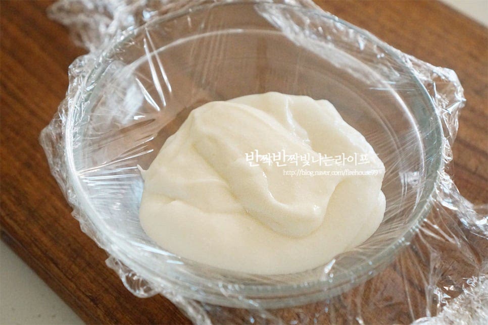 깊이감이 있는 볼에 랩을 씌운 뒤 그 위로 적당량을 덜어 올려줍니다. 굳지 않게 모양을 잡아주세요. 랩으로 감싸 동그란 모양을 만들어줍니다. 뜨거울 때 모양을 내어주어야 굳지 않고 곱게 동그랗게 만들어져요. 기포 부분이 생기지 않게 손으로 콕콕 눌러 공기를 빼준 뒤 고정해 줍니다. 그리고 얼음물에 담가 열기를 식혀주어요. 비닐랩과 얼음물을 미리 준비해두면 보다 빠르게 요리할 수 있습니다. 차갑게 식힌 뒤 냉장고에서 3~4시간 굳혀 쫀득하게 만들어줍니다.