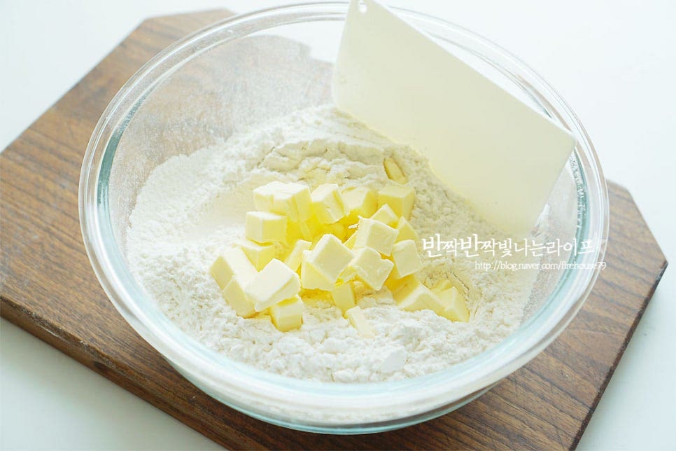 박력분 300g, 베이킹파우더 7g 설탕 55g, 소금 2g 가루 재료는 체에 내려준 뒤 차가운 버터를 넣어줍니다. 여기서 중요한 팁은 차가운 상태의 버터입니다. 버터가 녹지 않도록 반죽을 빠르게 만들어 줄 것이에요. *반죽을 섞기 좋도록 버터는 큐브 모양으로 잘라 준비했어요. 스크래퍼로 버터를 잘게 잘라주어 섞어줍니다. 손이 닿으면 버터가 녹으니 스크래퍼 또는 푸드프로세서로 반죽을 섞어주어요. 작은 쌀알 크기로 보슬보슬한 상태로 만들어 줍니다.