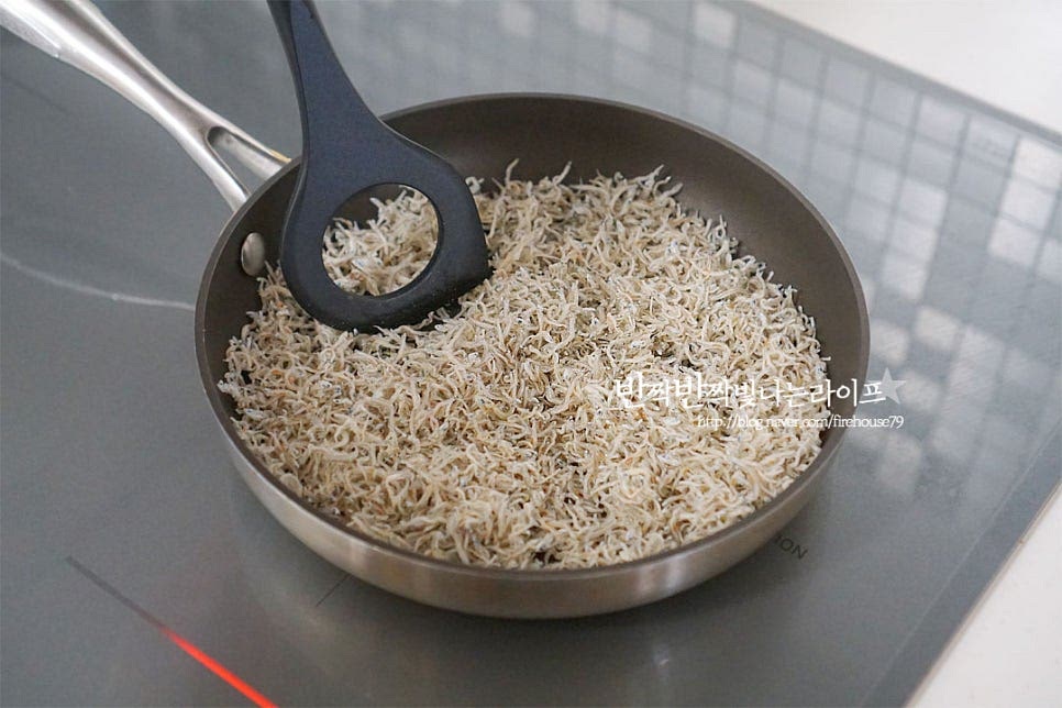 마른 팬에 멸치를 넣고 약불로 볶아 눅눅함을 날려줍니다. 보통 멸치 같은 경우 냉동실에 소분하여 두기 때문에 이렇게 먼저 볶아주시면 더 바삭바삭합니다. 볶다 보면 수분이 날아가면서 잔가루가 많이 나옵니다. 체에 밭쳐 잔가루는 털어줍니다. 잔가루를 털어내어주어야 더 깔끔한 맛을 낼 수 있습니다.