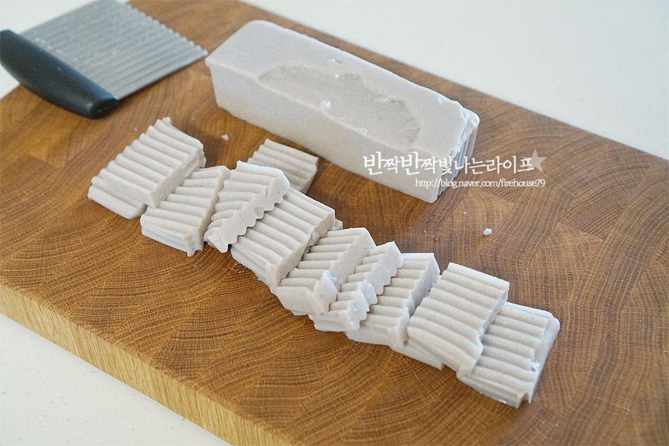 묵요리는 탱글탱글한 식감이 맛이 좋은데요. 냉장고에 두게 되면 녹말이 굳어 단단해질 수 있어 만져보았을 때 탱탱함이 없다면 끓는 물에 가볍게 데쳐주세요. 저는 뜨거운 물을 부어 헹구어 주었습니다. 길게 반으로 자른 뒤 1cm 두께로 썰어줍니다. 크기는 먹기 좋게 다르게 잘라주셔도 됩니다. 쪽파는 송송 썰어줍니다. 향긋하게 어우러지는 맛이 좋은데 부추나 대파를 넣어도 좋으며 매콤하게 먹고 싶다면 고추를 얇게 송송 잘라주세요.