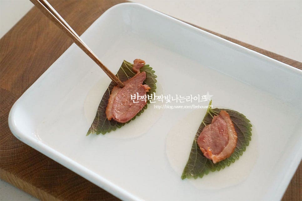 먼저 무쌈 위로 깻잎을 올려줍니다. 그 위로 훈제오리도 올려요. 채소와 고기가 어우러지면서 한입에 들어가는 쌈을 만든다고 생각하면 쉬워요. 색색이 채소도 올려줍니다. 색감을 맞추어 담아주면 말았을 때 더욱 먹음직스러워 보인답니다. 양쪽 부분을 잡고 부채모양으로 접어줍니다. 얇게 썰린 절인 무라 고정이 잘 된답니다. 쌈무말이를 만들 때 고정을 해주고 싶다면 데친 부추 또는 쪽파로 감싸 묶어주셔도 좋아요.