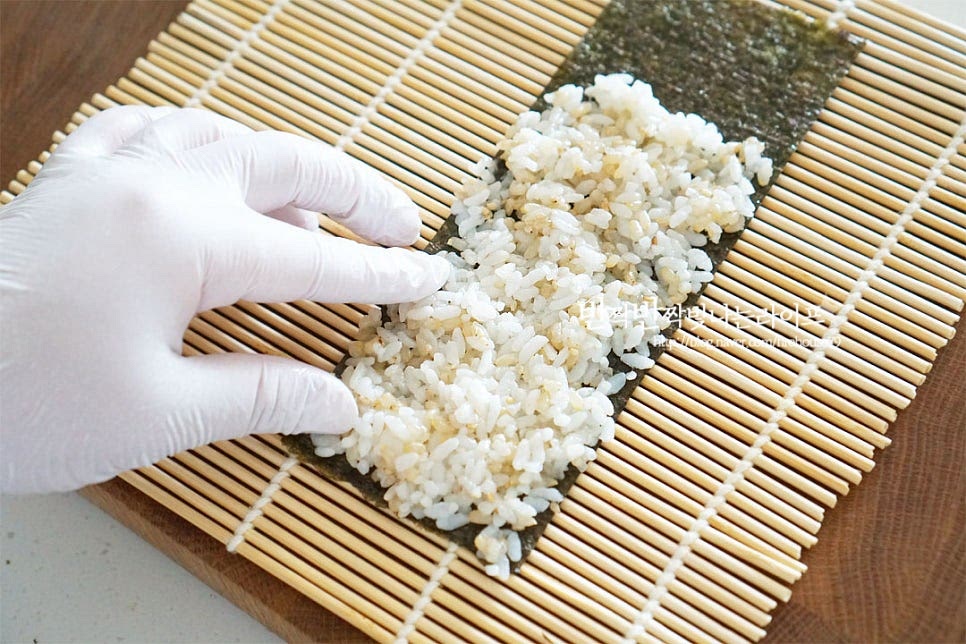 김을 먼저 깔고 그 위로 밥을 넓게 펼쳐 올려줍니다. 대략 2/3 정도까지 밥알을 뭉치지 않게 펼쳐주세요. 그 위로 깻잎을 깔고 치즈 - 계란지단 - 스팸 순으로 올려줍니다. 끝부분을 밥이 올려진 부분으로 말아 감싸줍니다. 동그랗게 말아 만드는 것이 아닌 사각김밥으로 말아서 만드는 김밥이라 처음 만들어보시는 분들도 어렵지 않게 말 수 있어요. 돌돌 말아준 뒤 고소하고 윤기가 나도록 참기름을 조씩 발라줍니다.