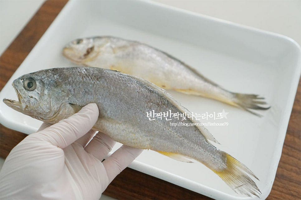 조기를 염장 건조한 것이라 먹기 좋게 소분하여 냉동실에 넣어두었어요. 차가운 쌀뜨물에 5분 정도 담가 해동하거나 미리 냉장실에 두어 해동해 주시면 됩니다. 쌀뜨물에 담글 때는 너무 오래 담그면 싱거워질 수 있으니 오래 담그지는 않도록 해주세요. 굽기 전 굴비 손질 먼저 해줍니다. 지느러미 부분은 가위로 다듬어 주어요. 칼로 비늘을 긁어 제거해 줍니다. 손질할 때 한 가지 중요한 게 내장을 제거해 주는 것인데요. 내장을 제거하지 않으면 쓴맛이 나고 구워지면서 흐물흐물 흘러내릴 수도 있는데요. 그렇기 때문에 제거한 뒤 구워주시는 게 좋아요. 아가미 부분으로 손을 넣어 배 부분에 내장을 당겨 빼준 뒤 흐르는 물에 헹구어 줍니다. 손질해 준 뒤 물기를 꼼꼼하게 제거해 줍니다. 물기가 있으면 굽다가 튈 수 있어요. 바삭바삭 속까지 맛있게 굽기 위해 칼집도 넣어줍니다.