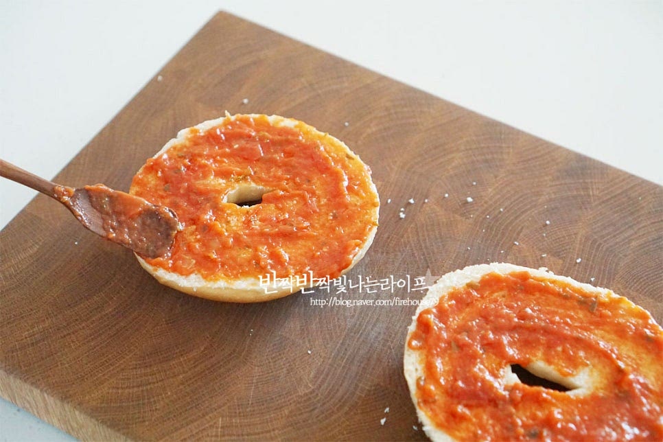 반으로 자른 빵 위에 토마토소스 1 큰 술씩 넓게 펼쳐 발라줍니다. 시판용 소스에 바질과 같은 향신 재료가 들어있어 따로 추가로 넣지는 않았는데 입맛에 따라 바질가루를 넣어도 맛있어요. 소스를 바른 베이글 위에 마요네즈를 버무린 토핑과 피자치즈를 올려줍니다. 가운데가 뚫린 모양이라 토핑이 흘러넘치지 않게 모양을 잡아주세요.