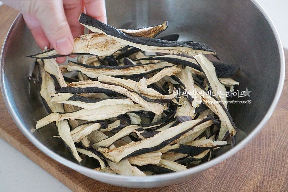 세척한 뒤 세로로 길게 썰어 말린 건가지는 생으로 먹을 때의 물컹한 식감과 달리 쫄깃하게 맛볼 수 있어 보름나물로 즐겨 먹곤 해요. 바삭하게 마른 상태로 반찬 만들기 좋도록 물에 불려줍니다. 넉넉하게 잠길 정도로 물을 부어줍니다. 이때 건조 상태에 따라 불리는 시간을 조절해 주는데요. 건나물 특유의 식감을 살리고 싶다면 1~2시간, 부드럽게 맛보고 싶다면 반나절 이상 불려주세요. 조금 더 빠르게 불리고 싶다면 미지근한 물에 담가주고요. 물 위로 뜨지 않도록 채반을 올려주면 물에 잠겨 불린답니다. 저는 아이랑 먹을 것이라 조금 부드럽게 먹고 싶어 반나절 정도 불려두었습니다. 중간에 상태를 확인하여 부드럽게 휘어지는 정도로 수분을 머금으면 서너 번 헹구어준 뒤 물기를 가볍게 짜줍니다. 껍질 부분이 조금 질기게 느껴질 수 있어 그 부분을 참고하여 불려주세요.