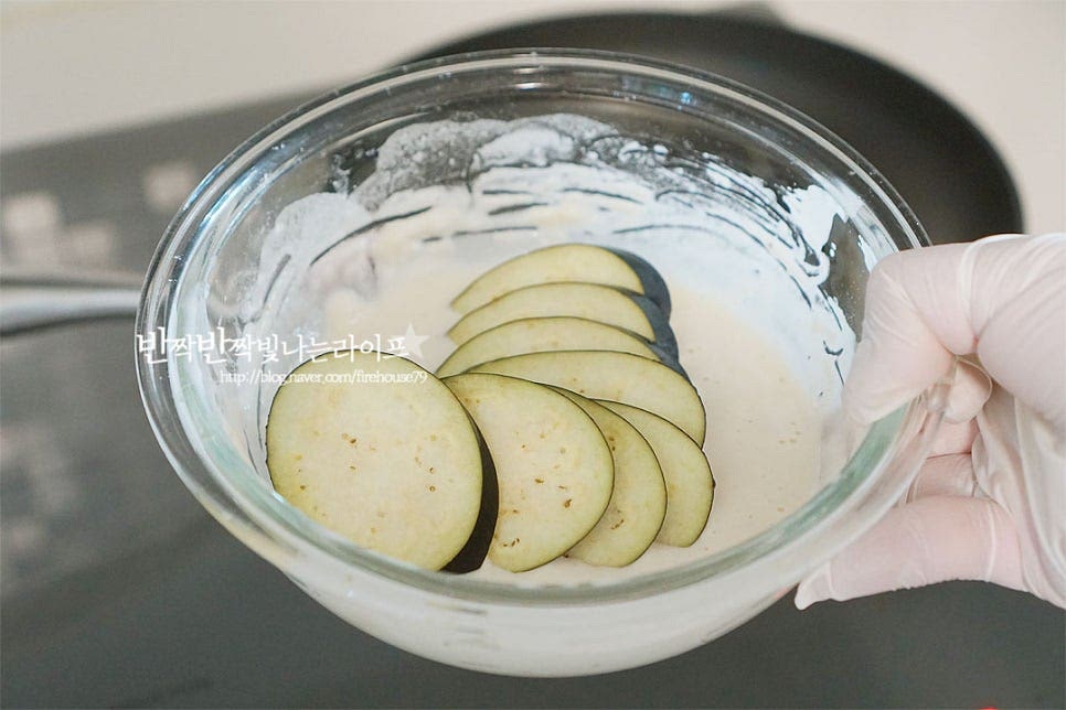 썰어둔 가지에 옷을 고르게 입혀줍니다. 프라이팬에 식용유를 자작하게 두르고 옷을 입힌 뒤 올려 전을 구워줍니다. 가지부침개는 기름에 튀기듯이 구워주면 고소한 풍미가 맛깔나요. 한쪽 면이 익으면 뒤집어 앞뒤로 노릇노릇하게 구워줍니다. 오래 익히지않아도 잘 구워지기 때문에 중간센불로 조절해 구웠습니다. 고소한 풍미에 굽는 모습만 보아도 식감과 향이 먹음직스러워요. 구운 뒤 눅눅해지지 않도록 공기가 통하는 체망에 올려 기름을 빼줍니다.