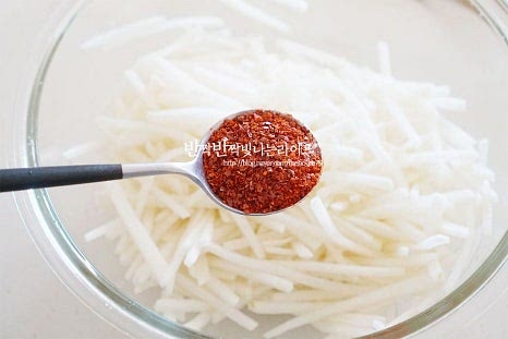 수분이 생겨서 촉촉한 상태 그대로 고춧가루 5 큰 술을 넣어줍니다. 설탕과 소금에 살짝 절여 생긴 수분을 어느 정도 잡아주면서 고춧가루가 물들면서 색을 빨갛게 내어줍니다. 식초 3 큰 술, 양조간장 2 큰 술, 액젓 1 큰 술을 넣어줍니다. 양조 또는 진간장을 넣어주면 되는데 검은색이 나지 않도록 테두리 부분으로 둘러서 넣어줍니다. 액젓은 까나리가 아닌 꽃게, 멸치 모두 좋습니다. 2배, 3배 식초를 사용한다면 양을 줄여 넣어줍니다. 양념이 더해질 수 있도록 무칩니다. 절인 뒤 양념을 해서 부서지지 않고 아삭합니다. 마지막으로 다진 대파도 넣어줍니다. 물이 생기면 싱거워질 수 있어 소금 1~2꼬집을 더해줍니다. 소금 간은 짜지 않도록 입맛에 맞게 조절해 주면 신맛과 단맛이 적당하게 어우러집니다. 새콤하게 먹는다면 식초를 추가해 주셔도 좋습니다. 재료가 모두 섞이도록 버무리면 어남 무생채 완성입니다.