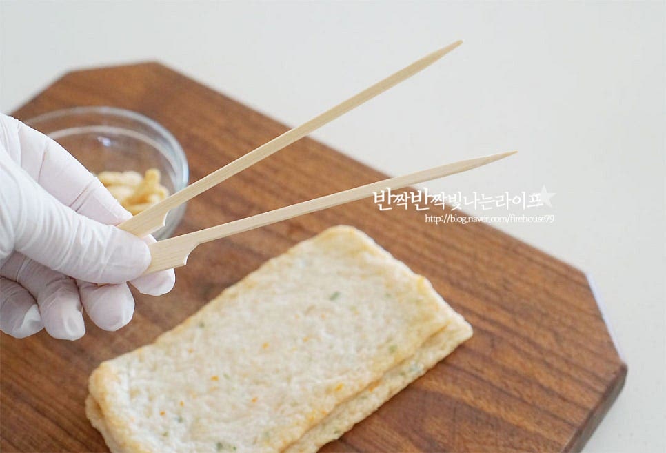 꼬치어묵을 먼저 만들어요. 시중에 쉽게 구할 수 있 나무꼬치를 준비했어요. 오뎅 양에 따라 크기는 맞추어 준비해 주세요. 반으로 잘라 꼬불 하게 모양을 잡아줍니다. 한입에 먹기 좋도록 길게 반으로 잘라 꼬불이를 만들어 주었어요. 꼬불이가 육수 맛이 잘 스며드는 편인데 취향에 따라 봉 모양 등 다양하게 준비해 주셔도 좋을 것 같아요. 꼬불하게 계단처럼 접어 나무에 끼워 줍니다. 육수에 넣어 끓이면서 끼운 게 풀릴 수가 있어 윗부분은 조금 여유 있게 모양을 잡아주었어요. 깔끔한 육수 맛을 위해 오뎅과 유부는 뜨거운 물을 부어 물기를 털어줍니다.