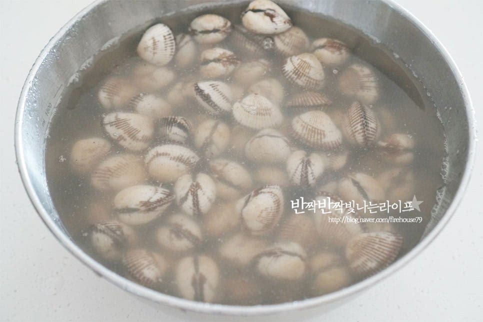 꼬막은 800g 정도를 준비했습니다. 뻘에서 나는 식재료라 생각보다 불순물이 꽤 많이 나오는 편이라 손질을 꼼꼼하게 해줍니다. 넉넉한 크기의 볼에 물과 담은 후 서너 번 정도 껍데기를 흔들어 세척해 줍니다. 너무 힘을 세게 주면 껍질이 깨질 수 있은 살짝 흔들어가며 씻어줍니다. 세척 후 해감을 하기 위해서 스테인리스 냄비 또는 볼에 꼬막이 잠길 정도로 물을 붓고 소금 1 큰 술을 넣고 녹인 다음 뚜껑을 덮거나 검은 비닐을 씌워 빛이 들어가지 않도록 차단하고 어둡고 서늘한 곳에서 1시간 정도 이상 해감해 줍니다. 날씨에 따라 냉장고에 넣어서 해감해 주고 스테인리스 소재를 사용하면 해감에 도움이 되며 저와 같이 냄비와 뚜껑을 활용하면 간편합니다. 1시간 이상 두었다가 열어보면 꼬막이 이물질을 뱉어내고 물이 뿌옇게 되어있습니다. 조개는 흐르는 물로 바락바락 문질러 깨끗한 물이 나올 정도로 세척한 뒤 채반에 밭쳐 물기를 털어줍니다.
