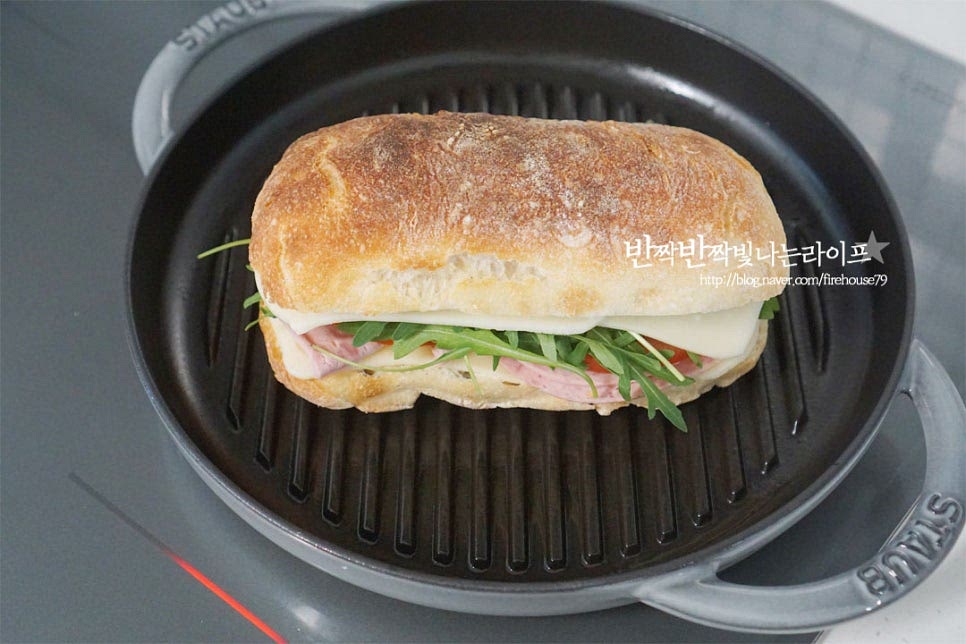 달군 그릴팬 위에 올려줍니다. 그릴팬에 구워 먹는 것이 정석이지만 상황에 따라 프라이팬에 구워도 좋습니다. 무거운 뚜껑으로 눌러 구워줍니다. 만드는 조리도구도 있지만 저와 같이 가끔 만들어 먹는다면 그릴팬과 무거운 뚜껑을 활용하면 집에서도 간단하게 요리 가능해요. 무게로 눌러지면서 재료가 데워지고 맛있게 구워집니다. 그릴 자국이 맛있게 생기고 치즈가 녹으면 완성입니다. 반으로 잘라보면 치즈가 쭉 늘어나면서 치아바타의 바삭바삭 식감이 더욱 돋보이며 속의 진한 감칠맛이 풍부합니다. 영상도 같이 담았어요. 치아바타를 반으로 자른 뒤 햄치즈와 루꼴라 토마토를 넣고 그릴팬에 따뜻하게 구워 먹는 레시피로 간단하고 맛이 좋습니다. 치아바타 샌드위치 만들기 따뜻하게 먹는 파니니샌드위치로 맛있게 요리해드세요. 끄읕 !