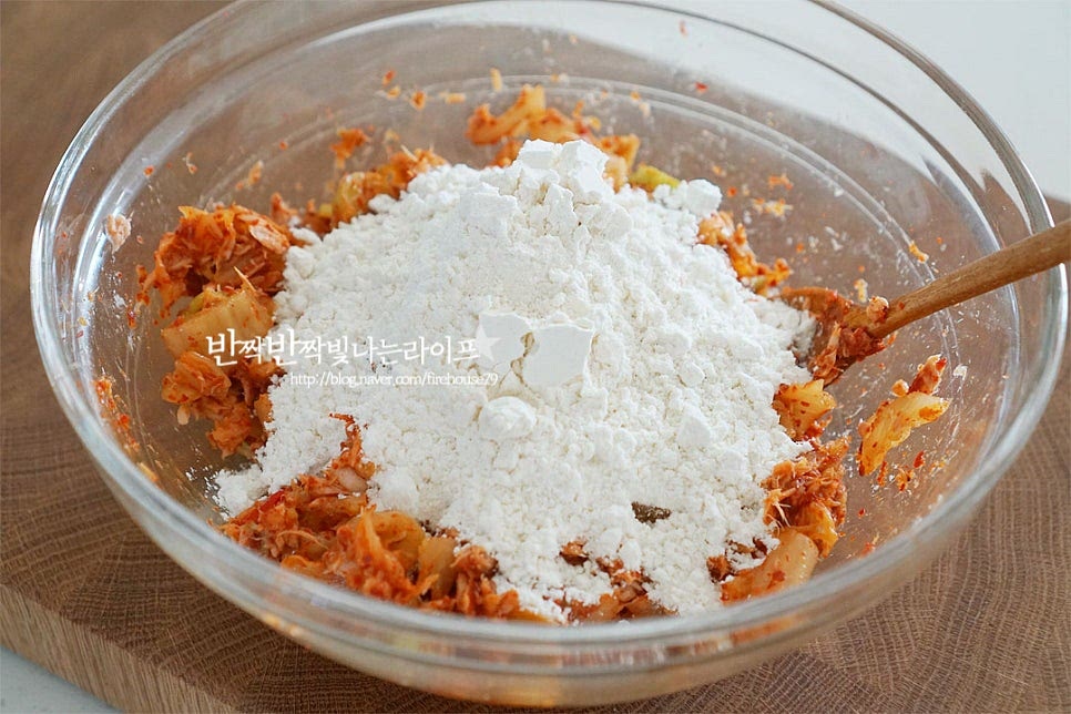 재료가 섞이면 부침가루 2컵을 넣어줍니다. 가루와 물을 1 : 1비율 정도로 잡아넣어주는데요. 재료에 수분이 있기 때문에 2컵에 차가운 물 1⅔ 컵을 부어줍니다. 차가운 물로 반죽을 만들어 뜨거운 기름에 구워주면 더욱 바삭 구울 수 있습니다. 바삭하게 굽기 위해서 섞을 때는 살살 저어가며 대충 섞는 느낌으로 저어주는데요. 부침가루에도 밀가루가 들어있어 너무 과하게 저어 섞게 되면 글루텐이 형성되어 찐득찐득하게 만들어질 수 있기 때문에 가능한 살살 저어가며 가볍게 섞어주세요. 섞어보았을 때 약간 묽은 듯한 농도인데요. 부침가루가 많이 들어가 뻑뻑하게 만들어지면 떡같이 구워지기 때문에 수분이 많은 정도가 기름이 자글자글하면서 튀겨지듯이 바삭한 맛이 난답니다.