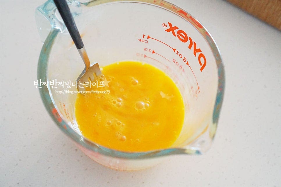 달걀은 덩어리 없이 곱게 풀어줍니다. 예열한 팬에 식용유 1/2 큰 술을 두르고 계란물을 넓게 펼쳐 부어줍니다. 테두리가 약간씩 익기 시작하면 밥을 올려줍니다. 반죽 정도 익으면 양쪽으로 밥을 감싸줍니다. 너무 익으면 고정이 되지 않으니 촉촉한 상태일 때 모양을 내어야 식감도 부드럽고 예쁘게 만들어집니다. 그릇에 옮겨 담은 뒤 키친타월 2~3장을 올려 양손으로 럭비공 모양으로 만들어줍니다.