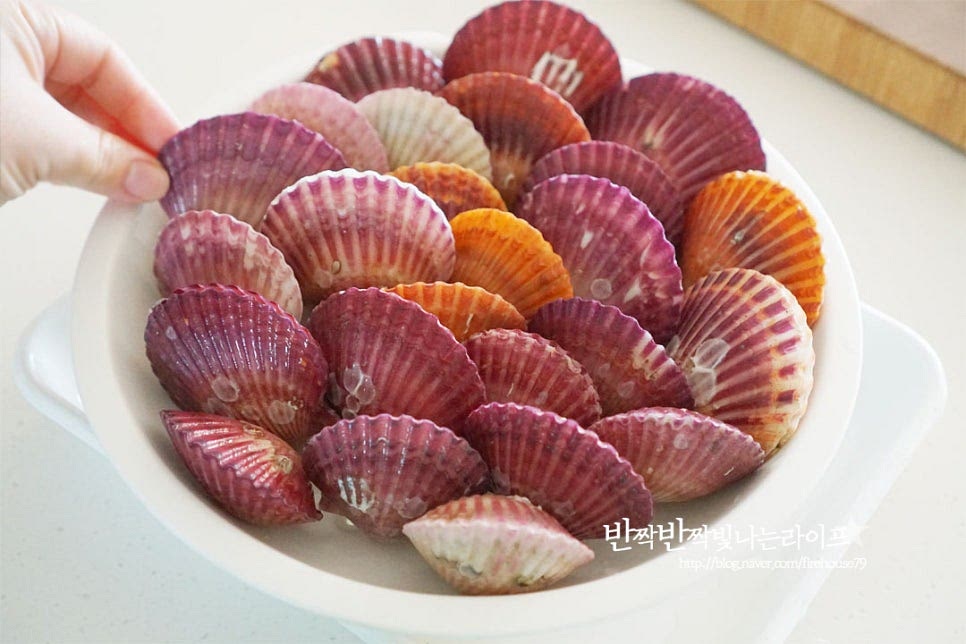 손질해준 뒤 찜기에 올려쪄주면 되어 정말 간단한 조리법으로 맛볼 수 있는데요. 본연의 풍미를 깊게 맛보고 탱글하면서 적당히 익어 질기지 않고 촉촉하며 비린내 없이 요리해 줍니다. 그러기 위해서 찜기에 올릴 때 열리는 부분이 위로 향하도록 세워줍니다. 그래야 맛있는 조개의 맛이 흘러내리지 않고 탱탱하게 익혀진답니다. 냄비에 물 200~300ml를 부어줍니다. 넘치지 않게 크기에 따라 물의 양을 조절해 주세요. 물이 팔팔 끓어오르면 그 위로 찜기를 올려줍니다. 찜기를 올리고 생강술(청주) 40ml를 부어줍니다. 비린내도 잡아주고 풍미를 살려준답니다. 가리비 찌는시간 뚜껑을 덮고 쪄줍니다. 찌는시간은 김이 오른 상태에서 10~15분 쪄줍니다. 크기나 양에 따라 시간을 조절해 주세요. 12분 정도 찐 뒤 5분 뜸을 들여 뚜껑을 열어보니 모두 입을 벌린 채 맛있게 익어있어요. 많이들 알고 있듯이 조개는 익었을 때 끝까지 입을 벌리지 않으면 신선한 것이 아니니 먹으면 안 됩니다. 입을 벌린 것은 조갯살만 발라 맛있게 먹음 되고요.