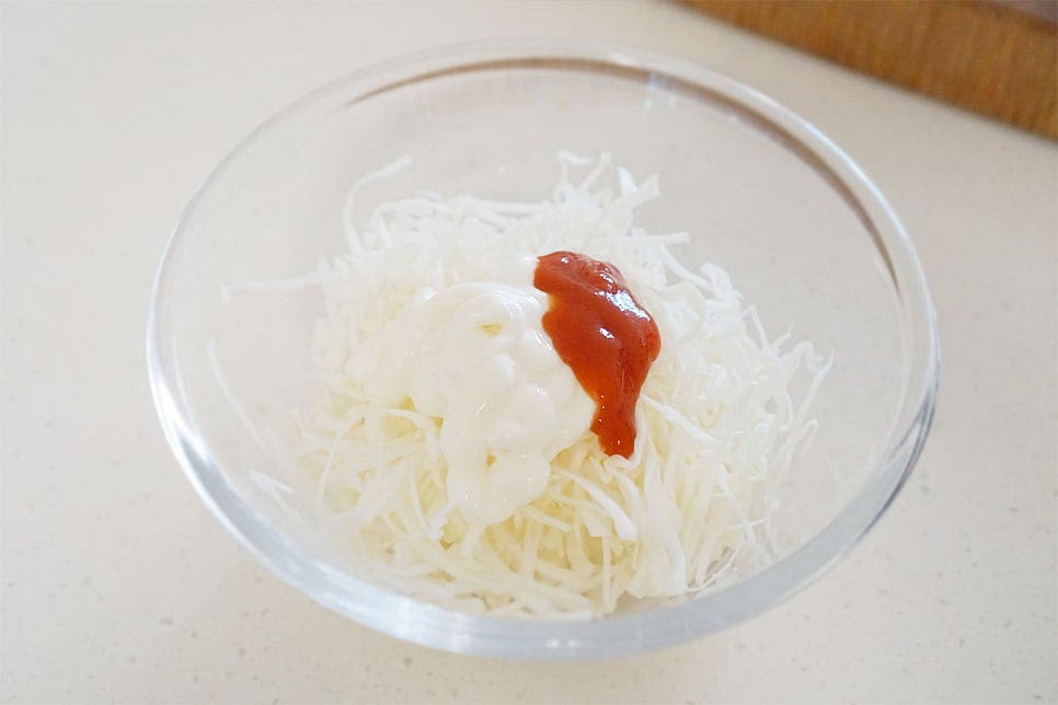 넉넉한 크기의 볼에 채 썬 양배추를 넣고 마요네즈 1½ 큰 술, 케첩 1 큰 술을 넣어줍니다. 케첩은 재료를 넣은 뒤 조금 더 뿌려줄 것이라 마요네즈보다 조금 적게 넣었습니다. 케요네즈가 재료와 잘 섞일 수 있도록 버무려줍니다. 케첩 마요네즈 소스는 양배추에 찰떡같이 어울리죠.
