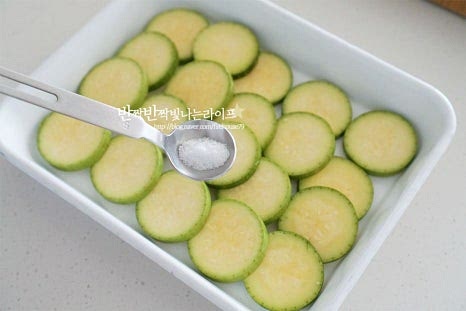 애호박전을 구울 때 두툼하게 썰어서 살짝 데쳐서 요리하기도 하는데 오늘은 소금 간을 먼저 해주어 간도 스며들고 식감도 아삭하고 단단하게 해준 뒤 달걀옷 입혀서 구워줄 것입니다. 소금 1/4 작은 술을 골고루 뿌려줍니다. 뭉치지 않게 살짝씩 뿌려주면 전체적으로 간이 됩니다. 소금을 뿌린 뒤 5~10분 정도 두면 밑간이 되면서 식감도 단단해지고 물방울이 생깁니다. 올라온 수분은 키친타월로 제거해 줍니다.