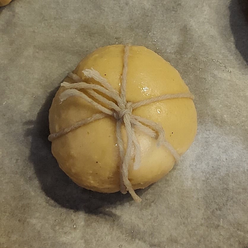 Shape the dough:
Divide the dough into 9 portions, weighing around 64g each.
Work each portion into a tight ball by circling it under your hand on a surface. Transfer each ball onto the prepared greaseproof papers and strings.
Carefully tie each piece of string around the donuts, loosely so that they only just stay in place, trying to keep the 6 segments even.
Cover with the oiled cling film and leave to rise until they're nearly doubled in size again - 45 minutes to 1hr15.