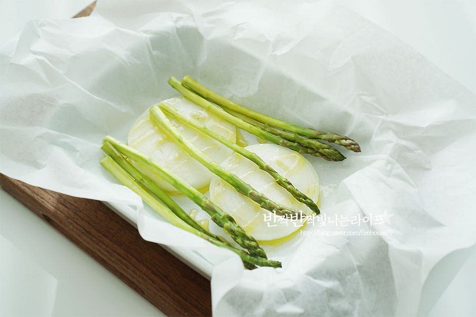 오븐용 그릇 위에 종이 포일을 크게 깔아줍니다. 재료를 모두 넣고 감싸줄 것이라 넉넉하게 잘라준비해요^^ 포일 위로 양파와 아스파라거스를 깔고 올리브오일 2 큰 술 정도 둘러줍니다. 양파 위로 생연어를 올려주어요. 먼저 양파를 깔고 올려주면 맛이 스며들어 더 잘 어우러진답니다. 소금, 후추 약간 뿌려 밑간하고 올리브오일 2 큰 술 정도 뿌려줍니다. 그리고 편으로 썬 마늘도 올려주고요. 바지락도 같이 넣어줍니다. 양송이버섯, 방울토마토도 같이 올려주어요. 가니시를 같이 넣고 익혀주는 것 같은 느낌으로 재료를 모두 같이 넣어주심 된답니다~ 레몬과 딜도 같이 넣어줍니다. 레몬이 들어가면 시트러스 한 특유의 향이 비린내도 잡아주고 향긋함을 살려주어요. 허브는 딜을 준비했는데 기호에 따라 타임, 오레가노 등 다양하게 곁들여주셔도 됩니다. 화이트와인 40ml를 가장자리로 뿌려줍니다. 와인 대신 청주도 좋아요~ 마지막으로 소금, 후추 약간 뿌린 뒤 버터 15g 올려줍니다. 버터가 들어가면 풍미가 더 깊어져요. 종이 포일로 감싸 재료가 새어나지 않도록 양 끝 부분을 밀봉하여 줍니다.