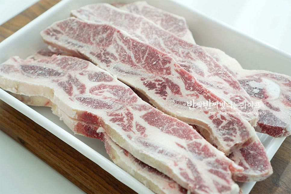 먼저 고기 핏물을 빼주는 것에서부터 시작인데요. 갈비는 썰리면서 뼛가루가 많이 묻어나기 때문에 깨끗하게 세척한 뒤 물에 담가 핏물을 빼줍니다. 흐르는 물에 씻어가며 겉면의 뼛가루를 제거해 주어요. 고기가 잠길 정도로 물을 부어 한 시간 정도 핏물을 빼주는데요. 양념에 핏물이 섞이지 않아야 누린내도 나지 않고 더 맛있게 구워드실 수 있어요. 저는 한 시간보다 넉넉하게 세 시간 담가주었고, 중간에 두세 번 물을 갈아 주었어요. 설탕 한 큰 술을 넣어주면 핏물을 보다 빠르게 뺄 수 있어요. 핏물을 제거한 뒤 씻어 물기를 털어줍니다.