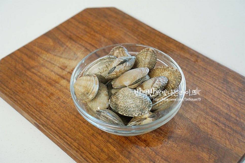 조개를 먹다가 이물질이 씹히면 손이 가지 않게 되는데요. 그만큼 재료를 해감 손질하는 과정이 중요해요. 해감만 잘해주면 끓이는 건 어렵지 않답니다. 먼저 물로 서너 번 바락바락 문질러 씻어줍니다. 껍질이 깨어지거나 상한 것은 골라내어주어요. 재료가 잠길 정도로 물을 붓고 소금 2 큰 술을 넣고 녹여줍니다. 대략 물 1L에 소금 2 큰 술 넣어주시면 되는데 바닷물과 같이 짠맛 농도를 맞추어준다고 생각하면 됩니다. 소금을 녹인 물에 넣고 해감해 주어요. 이물질을 뱉어낼 수 있도록 검은 비닐이나 신문지, 뚜껑을 덮어 빛이 들어가지 않고 어둡게 하여 조용하고 서늘한 곳에 한두 시간 둡니다. 마트에서 구입하는 것은 어느 정도 손질이 된 상태라 두 시간 정도면 충분한데 손질이 되지 않은 것은 반나절 이상 두셔야 합니다. 두 시간 정도 둔 뒤 뚜껑을 열어보니 열심히 움직이고 있더라고요. 이물질도 꽤 나온 상태에요. 흐르는 물에 깨끗하게 씻어줍니다. 손질한 뒤 체에 밭쳐 가볍게 물기를 털어주시면 되어요.