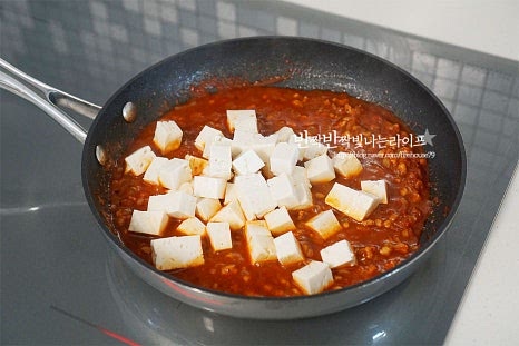 재료가 어우러지면 두부를 넣어줍니다. 전분물을 둘러 넣어 골고루 섞어줍니다. 뭉치지않게 풀어 섞어주고 농도에 따라 전분물을 조절해 주세요. 참기름을 둘러 마무리합니다. 밥 위에 마파두부를 올린 뒤 쪽파로 마무리 완성합니다.