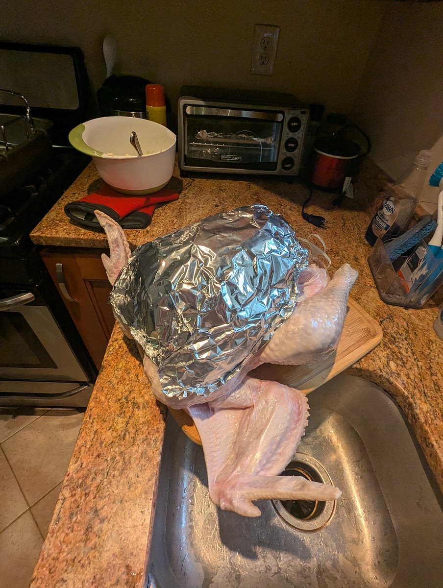 Preparing the turkey for the oven.
Firstly when the turkey comes out of its dry salt bath, start preheating the oven to 500° Fahrenheit, then remove & discard the paper towels & clean the bucket.
Then brush off any excess salt with paper towels & place the bird on a clean work surface & take it's legs temporarily out of its plastic stirrups.
You will then have to break all of the skin on the turkey, free of the meat. We do this by putting a hand under the skin (from the exposed neck cavity) & working around until all of the breast & thigh skin is loosened. (This is important for the next step of buttering the turkey) Also at this time, I like to shape the aluminum foil breast plate for the second phase of roasting.
To do this I take about a 2 foot piece of heavy duty aluminum foil & fold it in half with a slight angle, almost to form a V or heart. Then shape it over the breast of the turkey (with the split of the V going over the top of the breast & the fold at the bottom).
I then fold & crinkle the edges back until it is fully formed.
The goal being to cover all of the breast meat, but not the thigh) as the plate will go on after the first phase of roasting to reflect heat from the breast & allow the white meats to cook slower than that of the legs/thighs. I then remove the plate to be applied later.