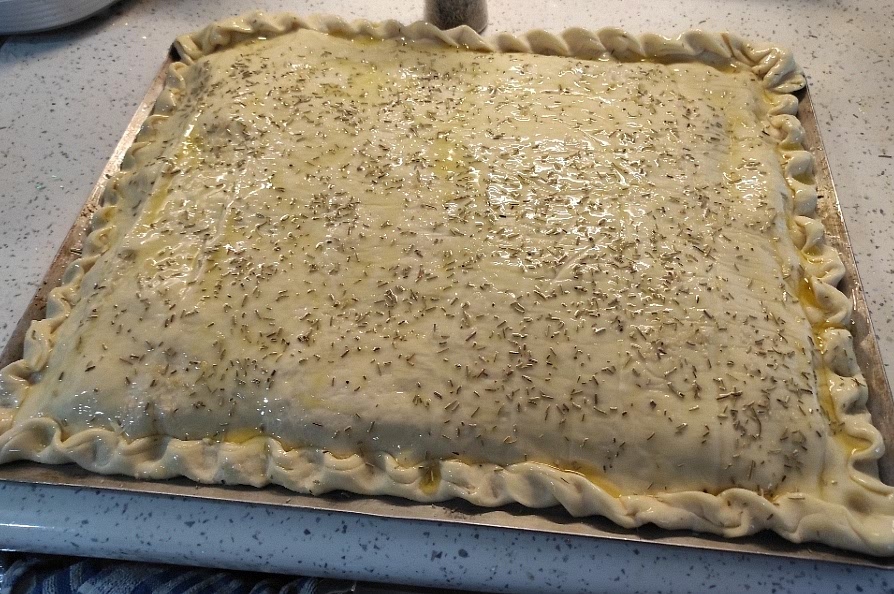 Cubrir con la otra mitad de la masa y cerrar el perímetro repulgando los bordes como una empanada. Dejar reposar cubierto con un paño de cocina. Hacer un hueco en el medio para que escape el vapor durante la cocción, con un pincel untar generosamente de aceite de oliva, esparcir sal gorda y opcionalmente romero.