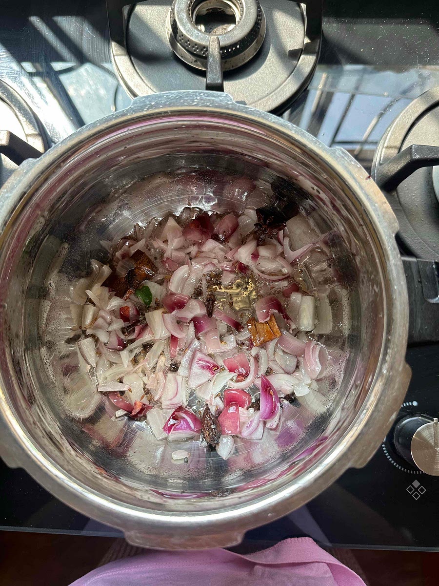 Once the rai splitters, add chopped red onions and curry leaves.