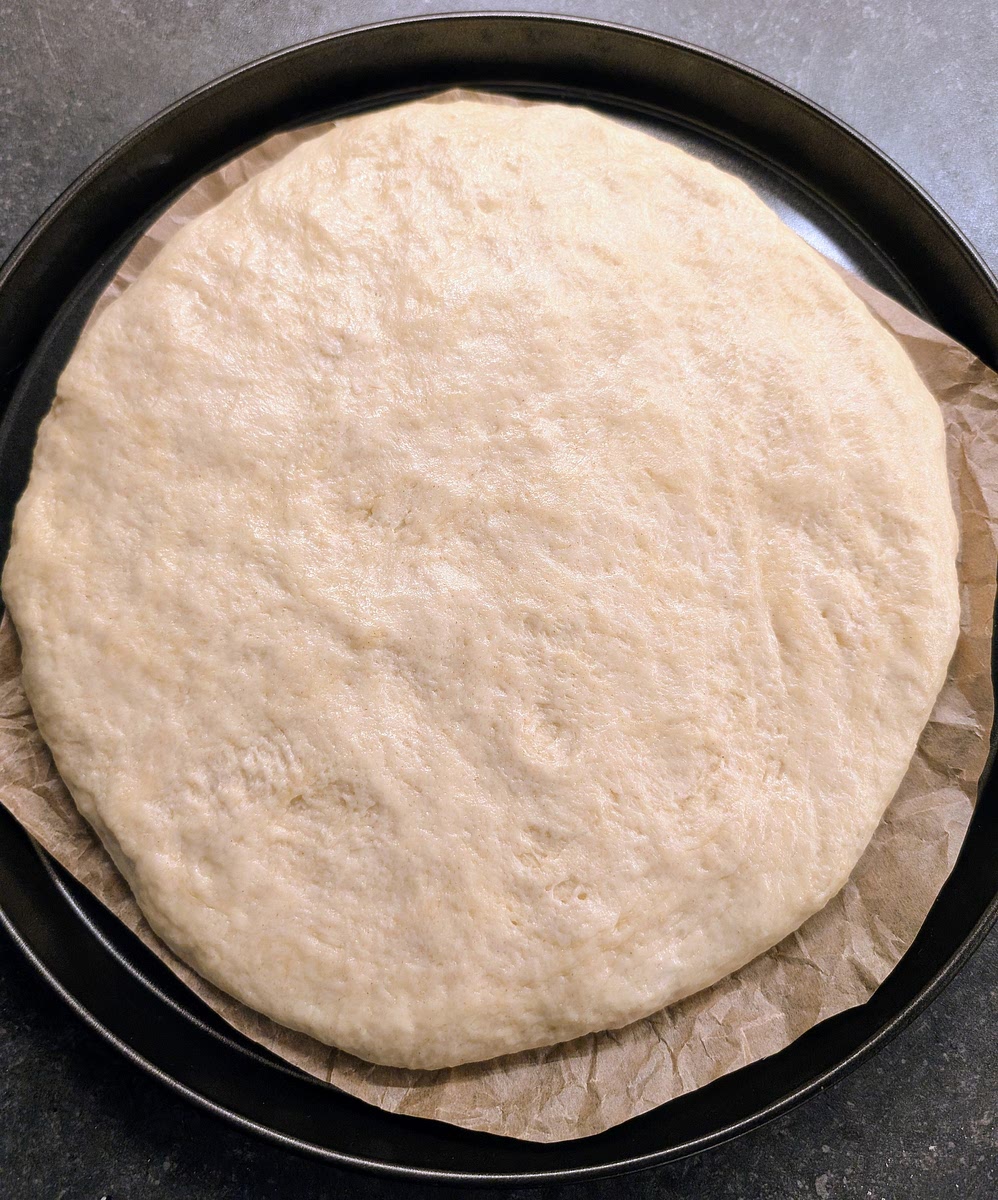 Stretch and flatten the dough with your hands over the parchment paper, leaving about 1 ½ cm from the edge of the pan free of dough.